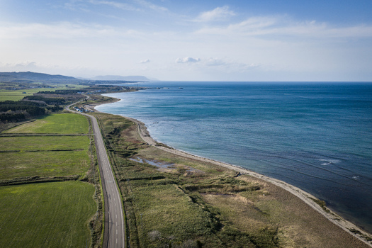 Aerial view of the coastal road winding along the green fields and the blue sea in Wakkanai Hokkaido Japan.