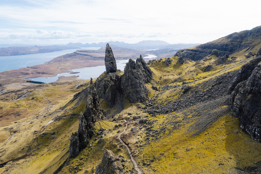 Aerial view of The Storr a dramatic rocky pinnacle on the Isle of Skye with rugged grassy slopes hiking trails and coastal waters in Portree Scotland United Kingdom. Aerial view of The Storr a dramatic rocky pinnacle on the Isle of Skye with rugged grassy slopes hiking trails and coastal waters in Portree Scotland United Kingdom.