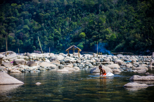 Meghalaya India 31 March 2023 View of a young boy playing in the clear waters of a rocky river surrounded by lush green forests and traditional bamboo structures in the background. Meghalaya India 31 March 2023 View of a young boy playing in the clear waters of a rocky river surrounded by lush green forests and traditional bamboo structures in the background.
