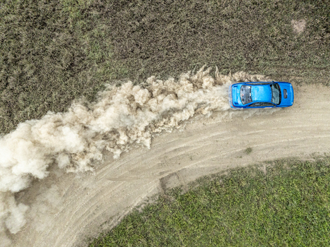 Aerial view of a blue rally car speeding on a dirt track and kicking up a massive cloud of dust in the Swara Plains Conservancy Nairobi Machakos County Kenya. Aerial view of a blue rally car speeding on a dirt track and kicking up a massive cloud of dust in the Swara Plains Conservancy Nairobi Machakos County Kenya.