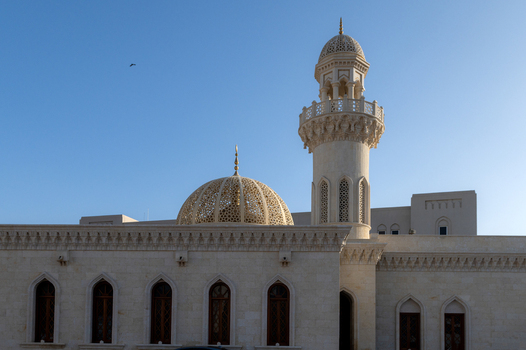 View of a beautiful mosque featuring an intricate golden dome and a tall minaret against a clear blue sky in Muscat Muscat Governorate Oman. View of a beautiful mosque featuring an intricate golden dome and a tall minaret against a clear blue sky in Muscat Muscat Governorate Oman.
