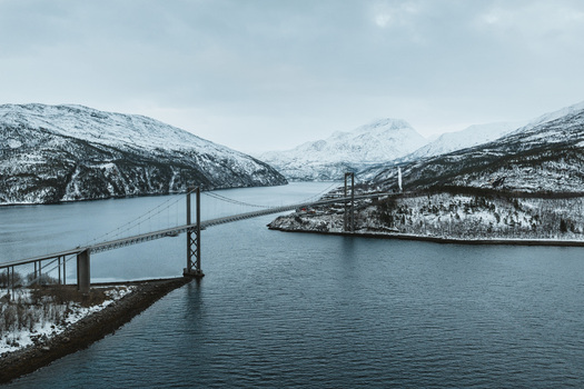 Aerial view of a bridge spanning a fjord connecting snow dusted mountain landscapes under a cloudy sky Troms&oslash; Norway.