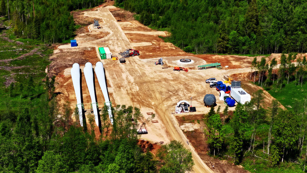 Aerial view of a wind turbine foundation construction site with large turbine blades heavy machinery and shipping containers in a forest clearing in Latvia. Aerial view of a wind turbine foundation construction site with large turbine blades heavy machinery and shipping containers in a forest clearing in Latvia.