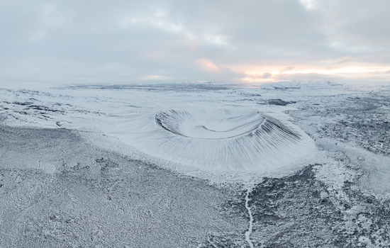 Aerial view of Hverfjall crater covered in snow with rugged volcanic terrain and soft light under a cloudy sky in Thingeyjarsveit Iceland. Aerial view of Hverfjall crater covered in snow with rugged volcanic terrain and soft light under a cloudy sky in Thingeyjarsveit Iceland.