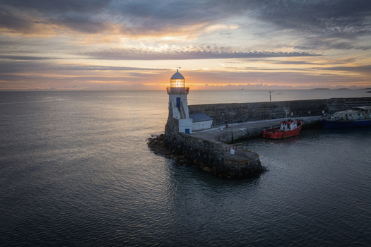 Aerial view of Balbriggan Lighthouse at the end of a stone pier with a red boat docked during a vibrant sunrise Balbriggan County Dublin Ireland. Aerial view of Balbriggan Lighthouse at the end of a stone pier with a red boat docked during a vibrant sunrise Balbriggan County Dublin Ireland.