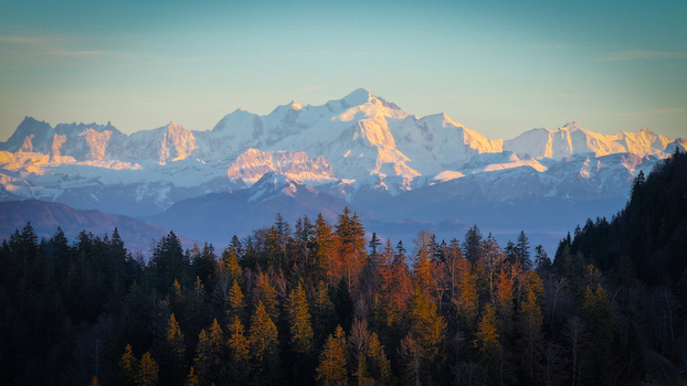 Aerial view of the Mont Blanc massif with snow covered peaks and dense evergreen forest under a clear sky at sunset in Chamonix Auvergne Rhone Alpes France. Aerial view of the Mont Blanc massif with snow covered peaks and dense evergreen forest under a clear sky at sunset in Chamonix Auvergne Rhone Alpes France.