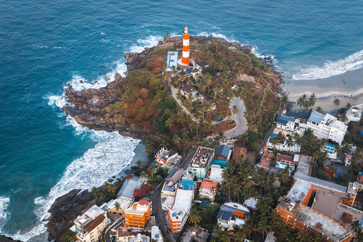 Aerial view of Vizhinjam Lighthouse situated on a rocky cliff surrounded by lush palm trees coastal buildings and the blue waters of the Arabian Sea in Kovalam Keralam India. Aerial view of Vizhinjam Lighthouse situated on a rocky cliff surrounded by lush palm trees coastal buildings and the blue waters of the Arabian Sea in Kovalam Keralam India.