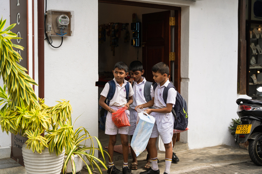 Sri Lanka 07 January 2026 View of three schoolboys in white uniforms standing in a doorway of a white building with their school bags.