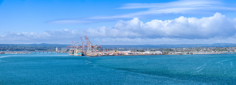 Aerial view of the Port of Tauranga with container ships and large industrial cranes under a bright blue sky Tauranga Bay of Plenty Region New Zealand.