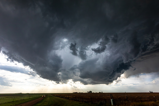 View of a dramatic supercell storm cloud looming over a vast flat rural landscape with a dirt road and a car illustrating severe weather in Oklahoma City Oklahoma United States.