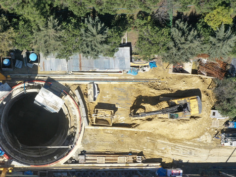 Aerial view of a construction site featuring a large circular shaft and a yellow excavator working on the dirt ground surrounded by green trees in Avcilar Istanbul Turkiye. Aerial view of a construction site featuring a large circular shaft and a yellow excavator working on the dirt ground surrounded by green trees in Avcilar Istanbul Turkiye.