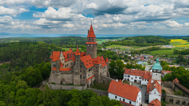 Aerial view of Bouzov Castle with its iconic red roofs and tall tower surrounded by lush green forests and rolling hills Bouzov Olomoucky kraj Czechia. Aerial view of Bouzov Castle with its iconic red roofs and tall tower surrounded by lush green forests and rolling hills Bouzov Olomoucky kraj Czechia.