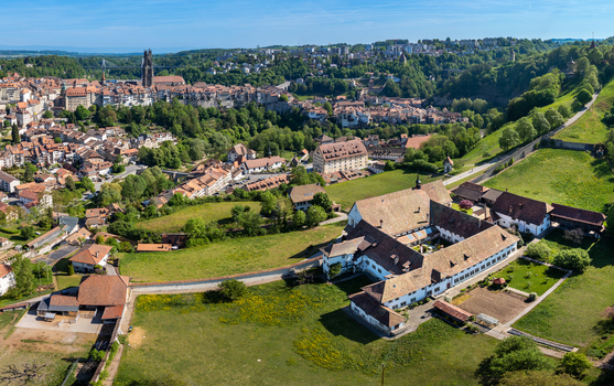 Aerial view of the Monastere de Montorge surrounded by green meadows with the historic city of Fribourg and its cathedral in the background under a clear blue sky Fribourg Fribourg Switzerland.