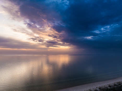 Aerial view of the calm Baltic Sea coastline at Perkone during a dramatic sunset with golden light reflecting on the water under dark clouds in Grinvalti South Kurzeme Municipality Latvia. Aerial view of the calm Baltic Sea coastline at Perkone during a dramatic sunset with golden light reflecting on the water under dark clouds in Grinvalti South Kurzeme Municipality Latvia.