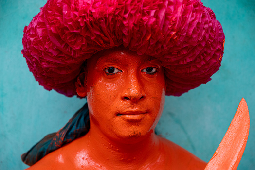 Munshiganj Bangladesh 13 April 2026 View of a man with his face and body painted orange wearing a large pink ruffled headpiece and holding a wooden sword during a traditional festival.