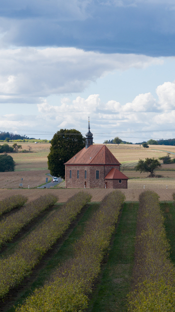 Aerial view of Wendelinuskapelle surrounded by agricultural fields and rolling hills under a cloudy sky in Monchberg Bayern Germany. Aerial view of Wendelinuskapelle surrounded by agricultural fields and rolling hills under a cloudy sky in Monchberg Bayern Germany.