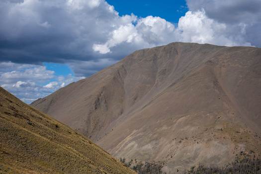 View of San Luis Peak featuring rugged mountain slopes covered in dry grasses under a cloudy blue sky in Creede Colorado United States. View of San Luis Peak featuring rugged mountain slopes covered in dry grasses under a cloudy blue sky in Creede Colorado United States.