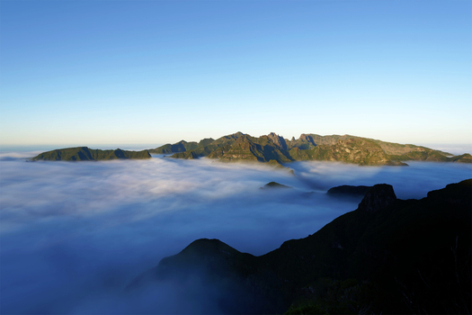 Aerial view of Bica da Cana peak rising above a sea of clouds under a clear blue sky in Madeira Portugal.