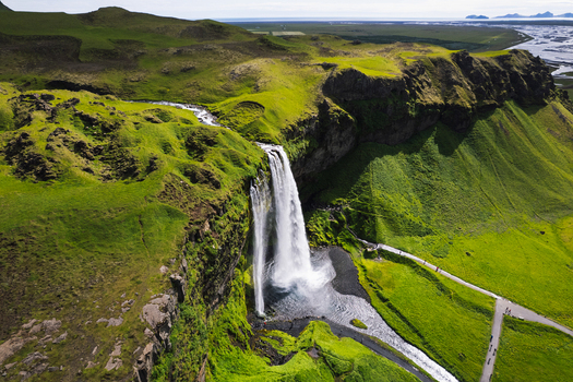Aerial view of Seljalandsfoss waterfall cascading over a steep mossy cliff into a pool with walking paths and green meadows Rangarthing eystra Iceland. Aerial view of Seljalandsfoss waterfall cascading over a steep mossy cliff into a pool with walking paths and green meadows Rangarthing eystra Iceland.