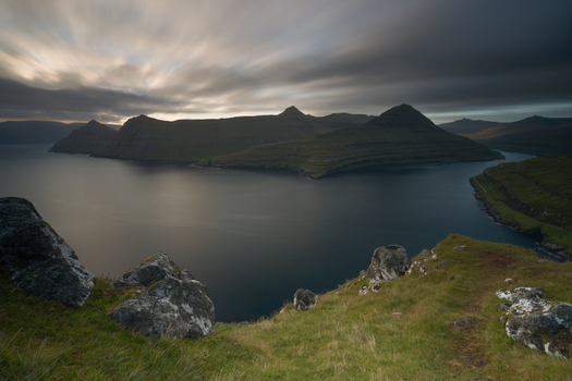 View of the dramatic mountains and calm waters of a fjord in the Faroe Islands. View of the dramatic mountains and calm waters of a fjord in the Faroe Islands.
