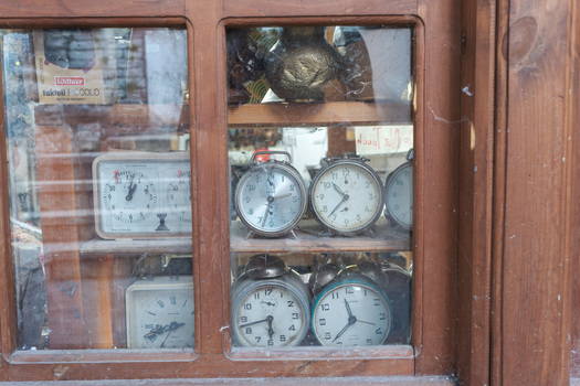 Gjirokaster Albania 09 June 2026 View of vintage alarm clocks and a chess clock displayed behind a dusty wooden window in the old town of Gjirokaster Albania.