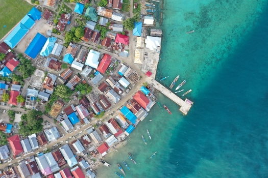 Aerial view of Pulau Maginti village with colorful rooftops a wooden pier and small boats moored in the turquoise coastal waters of Maginti South East Sulawesi Indonesia.