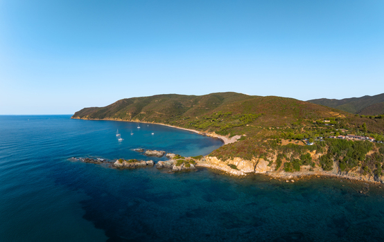 Aerial view of Lacona Beach with its turquoise waters rocky shoreline and lush green hills under a clear blue sky in Lacona Tuscany Italy.