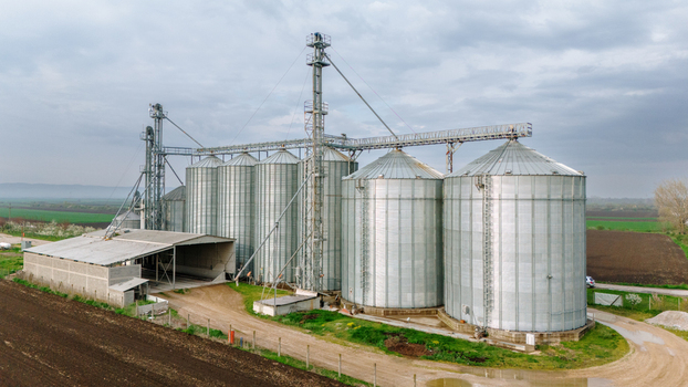 Aerial view of gleaming metallic silos stand against the backdrop of a cloudy sky contrasting with the dark earth and budding fields Sremska Mitrovica Vojvodina Serbia. Aerial view of gleaming metallic silos stand against the backdrop of a cloudy sky contrasting with the dark earth and budding fields Sremska Mitrovica Vojvodina Serbia.