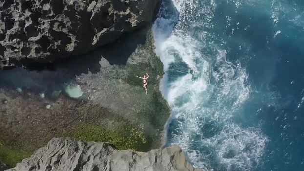 Aerial view of a woman lying on a rocky cliff with crashing waves Indonesia. Aerial view of a woman lying on a rocky cliff with crashing waves Indonesia.