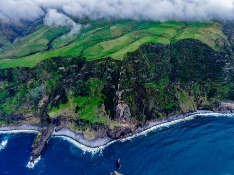 Aerial view of the rugged coastline meets the sapphire sea crowned by emerald hills under a misty veil Flores A&ccedil;ores Portugal.