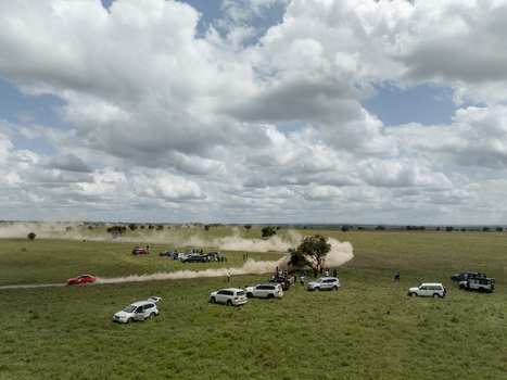 Aerial view of Swara Plains Conservancy with a red rally car racing on a dirt track kicking up dust surrounded by parked vehicles and people in Nairobi Machakos County Kenya. Aerial view of Swara Plains Conservancy with a red rally car racing on a dirt track kicking up dust surrounded by parked vehicles and people in Nairobi Machakos County Kenya.