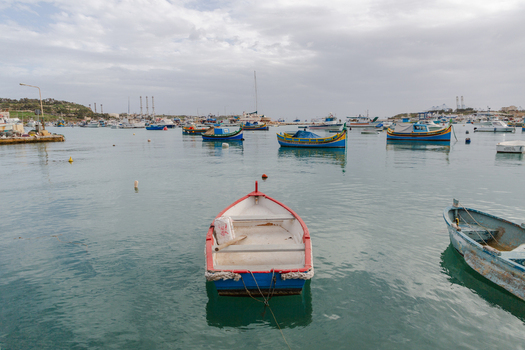 View of colorful traditional fishing boats bobbing gently on the tranquil water in a quaint harbor under a cloudy sky Marsaxlokk Malta. View of colorful traditional fishing boats bobbing gently on the tranquil water in a quaint harbor under a cloudy sky Marsaxlokk Malta.