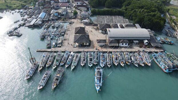 Aerial view of the bustling Bakauheni fishing harbor with numerous wooden boats moored at the pier adjacent to coastal buildings in Bakauheni Lampung Indonesia.