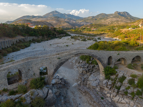Aerial view of Mesi Bridge spanning a dry riverbed with stone arches and surrounding rocky landscape in Boks Qarku i Shkodres Albania.