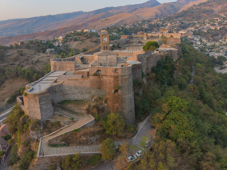 Aerial view of Gjirokaster Fortress with its iconic clock tower stone walls and historic town architecture set against the rugged mountains of Gjirokaster Gjirokaster County Albania. Aerial view of Gjirokaster Fortress with its iconic clock tower stone walls and historic town architecture set against the rugged mountains of Gjirokaster Gjirokaster County Albania.