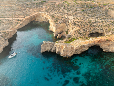 Aerial view of the Blue Lagoon s turquoise waters meeting the rugged sun baked cliffs a solitary boat gliding through the serene bay Comino Malta. Aerial view of the Blue Lagoon s turquoise waters meeting the rugged sun baked cliffs a solitary boat gliding through the serene bay Comino Malta.