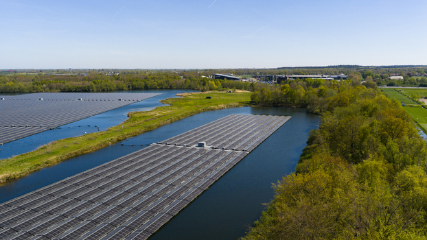 Aerial view of floating solar panels on a lake surrounded by lush green trees and fields under a clear blue sky in Zwolle Overijssel Netherlands. Aerial view of floating solar panels on a lake surrounded by lush green trees and fields under a clear blue sky in Zwolle Overijssel Netherlands.