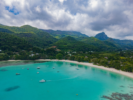 Aerial view of turquoise waters meeting the soft sandy beach with lush green hills rising in the background Port Launay Mahe Island Seychelles. Aerial view of turquoise waters meeting the soft sandy beach with lush green hills rising in the background Port Launay Mahe Island Seychelles.
