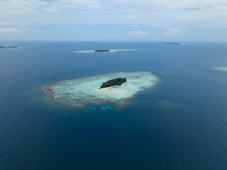 Aerial view of a small island surrounded by turquoise shallows contrasting with the deep blue ocean Cemara Kecil Island Karimunjawa Central Java Indonesia.