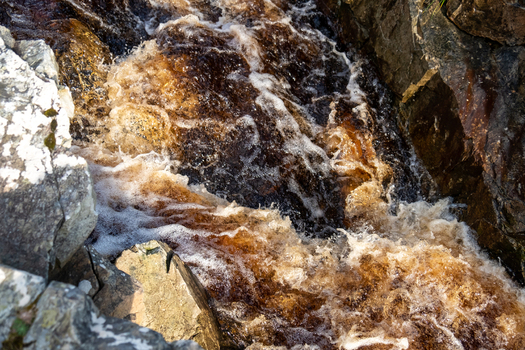 Aerial view of An Port waterfall with rushing peat stained water flowing over rugged dark rocks in Ardara County Donegal Ireland. Aerial view of An Port waterfall with rushing peat stained water flowing over rugged dark rocks in Ardara County Donegal Ireland.