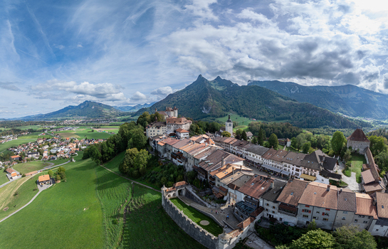 Aerial view of the historic Chateau de Gruyeres and the surrounding medieval town with traditional rooftops nestled in the green landscape in Gruyeres Fribourg Switzerland. Aerial view of the historic Chateau de Gruyeres and the surrounding medieval town with traditional rooftops nestled in the green landscape in Gruyeres Fribourg Switzerland.