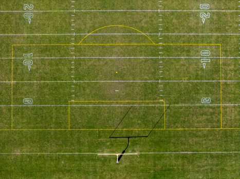 Aerial view of a football field with white yard lines and a goalpost casting a long shadow on the green grass in Kalamazoo Michigan United States. Aerial view of a football field with white yard lines and a goalpost casting a long shadow on the green grass in Kalamazoo Michigan United States.