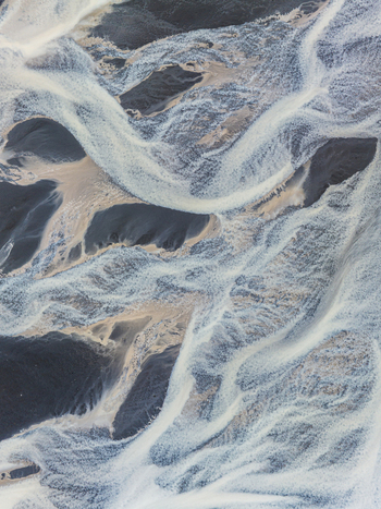 Aerial view of a glacial braided river with intricate patterns of white water flowing through dark volcanic sand in Iceland. Aerial view of a glacial braided river with intricate patterns of white water flowing through dark volcanic sand in Iceland.