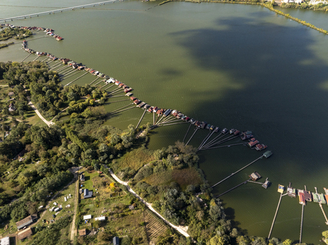 Aerial view of Bokodi Floating Village featuring colorful wooden houses on stilts connected by long wooden walkways over the lake in Oroszlany Hungary. Aerial view of Bokodi Floating Village featuring colorful wooden houses on stilts connected by long wooden walkways over the lake in Oroszlany Hungary.