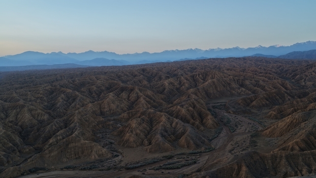 Aerial view of the rugged eroded landscape of Skazka Canyon with its intricate ridges and deep gullies set against distant snow capped mountains in Issyk Kul Region Kyrgyzstan. Aerial view of the rugged eroded landscape of Skazka Canyon with its intricate ridges and deep gullies set against distant snow capped mountains in Issyk Kul Region Kyrgyzstan.