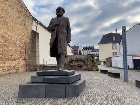 View of the Karl Marx statue standing in a cobblestone square with historic brick walls and urban buildings in the background in Trier Rheinland Pfalz Germany.