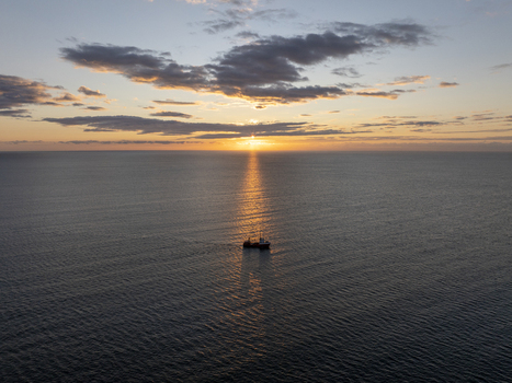 Aerial view of a small fishing boat sailing on the calm sea during a golden sunset near the historic town of Nessebar Burgas Bulgaria. Aerial view of a small fishing boat sailing on the calm sea during a golden sunset near the historic town of Nessebar Burgas Bulgaria.