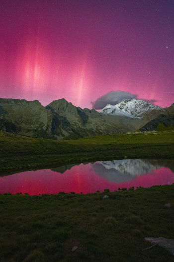 View of the vibrant pink aurora borealis over the snow capped peaks of Valtellina reflected in a calm alpine lake at night in Sondrio Lombardy Italy. View of the vibrant pink aurora borealis over the snow capped peaks of Valtellina reflected in a calm alpine lake at night in Sondrio Lombardy Italy.