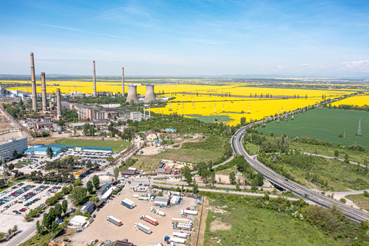 Aerial view of an industrial plant with tall chimneys and cooling towers next to vibrant yellow rapeseed fields and a highway in Ploiesti Prahova Romania. Aerial view of an industrial plant with tall chimneys and cooling towers next to vibrant yellow rapeseed fields and a highway in Ploiesti Prahova Romania.