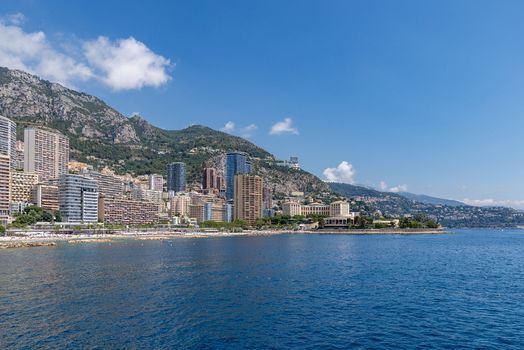 View of the coastal skyline of Monaco City featuring modern high rise buildings set against the mountains and the Mediterranean Sea in Monaco City Monaco. View of the coastal skyline of Monaco City featuring modern high rise buildings set against the mountains and the Mediterranean Sea in Monaco City Monaco.